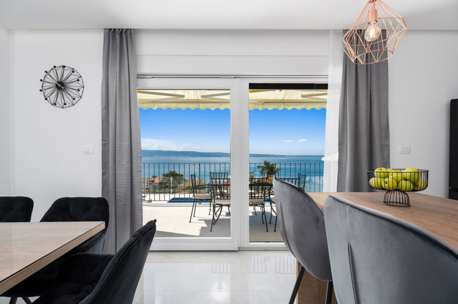 A living room with a sofa and a flat-screen TV also with a glass door toward the sun deck area.