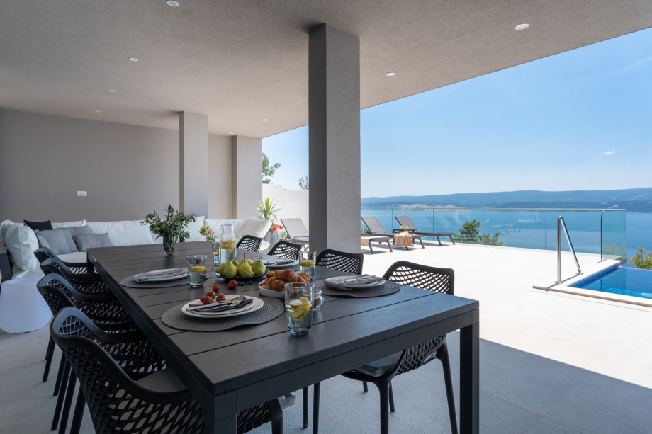 An open-plan living area with a covered outdoor dining area with BBQ, and a lounge corner.