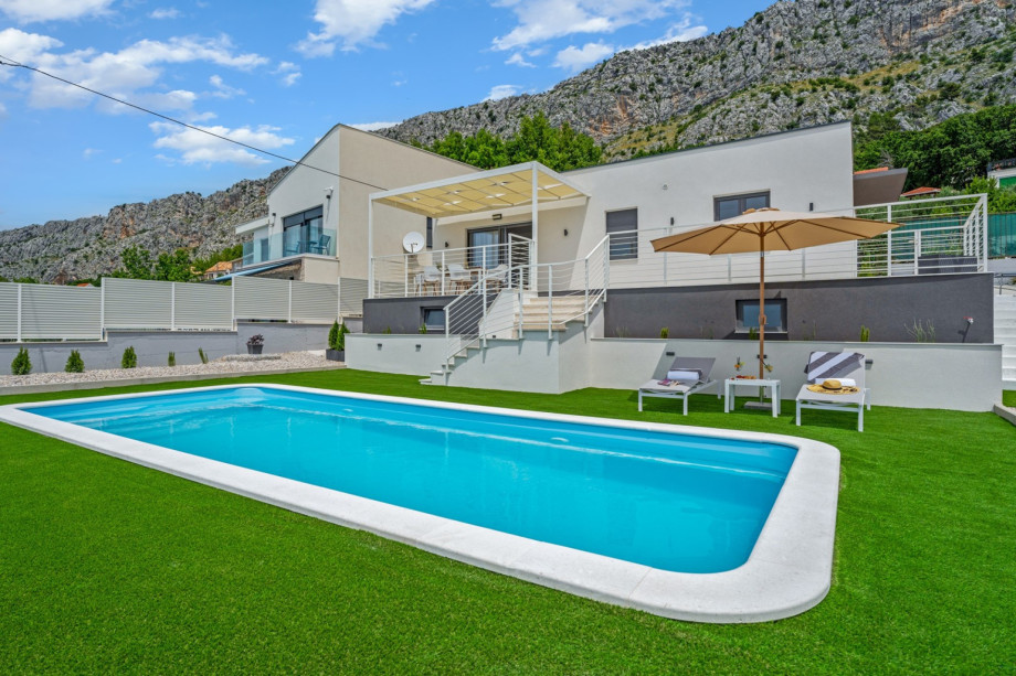 A private swimming pool 9m x 3,7m, a sun deck area with artificial grass and with 4 deck chairs, a lounge corner, an outdoor shower, and a sun umbrella