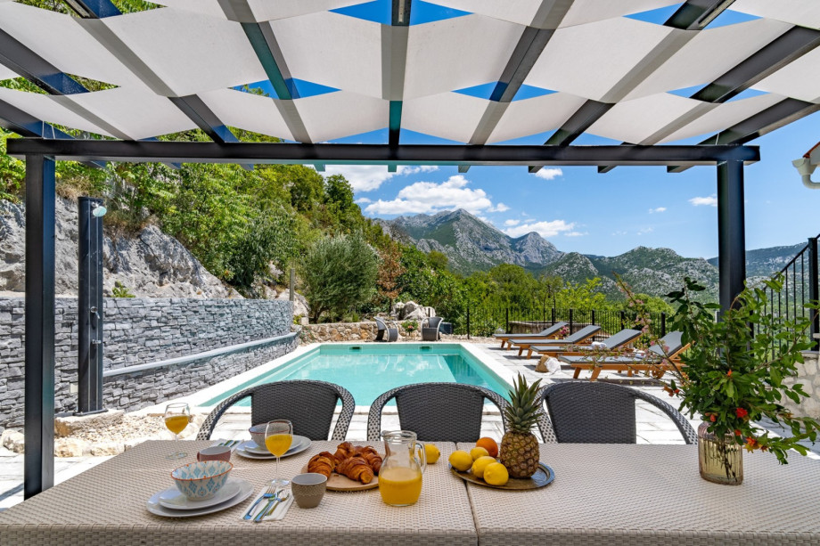 An outdoor dining area for 6 people, with a traditional barbecue, a fridge and 4 deck chairs, sun umbrella