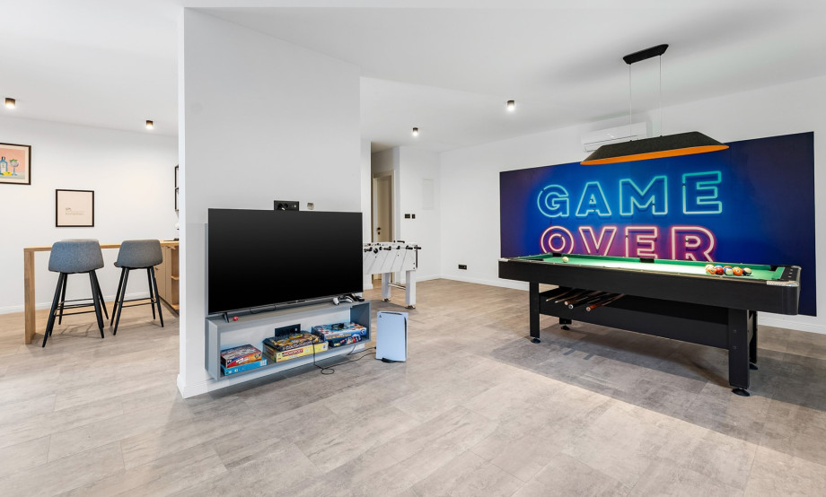A stylish entertainment space equipped with various board games, a flat-screen TV, bar stools, and classic games like pool and foosball, perfect for relaxing and having fun