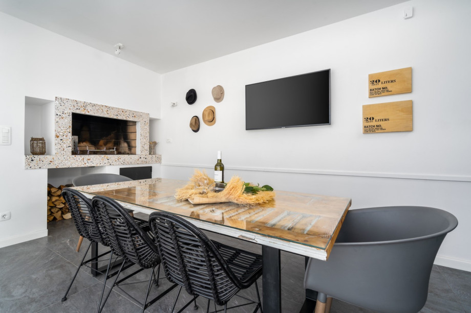 A summer kitchen with TV, barbecue, dining table for 8, and a toilet