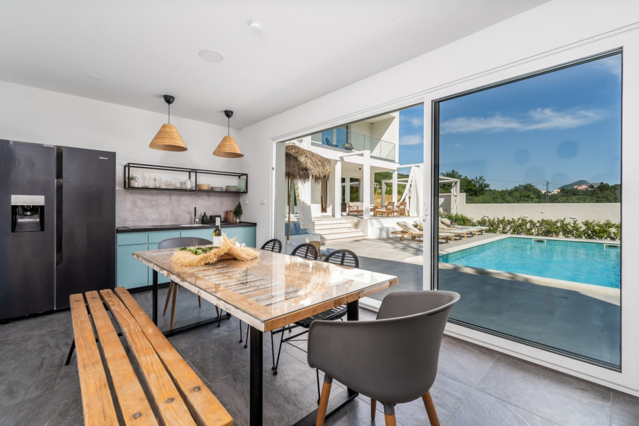 A  summer kitchen with TV, barbecue, dining table for 8, and a toilet