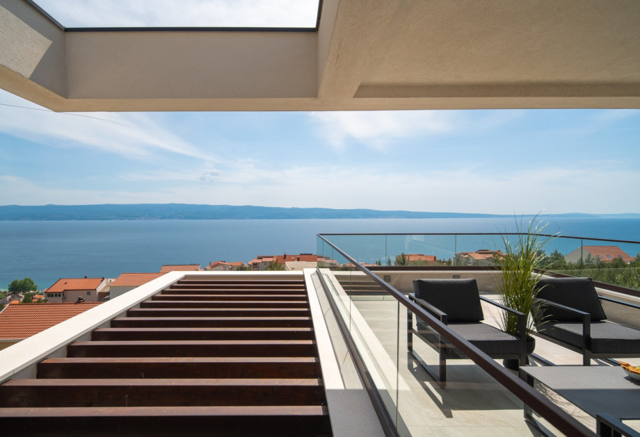 A spacious terrace with two chairs and deckchairs, perfect for enjoying the panoramic sea view.