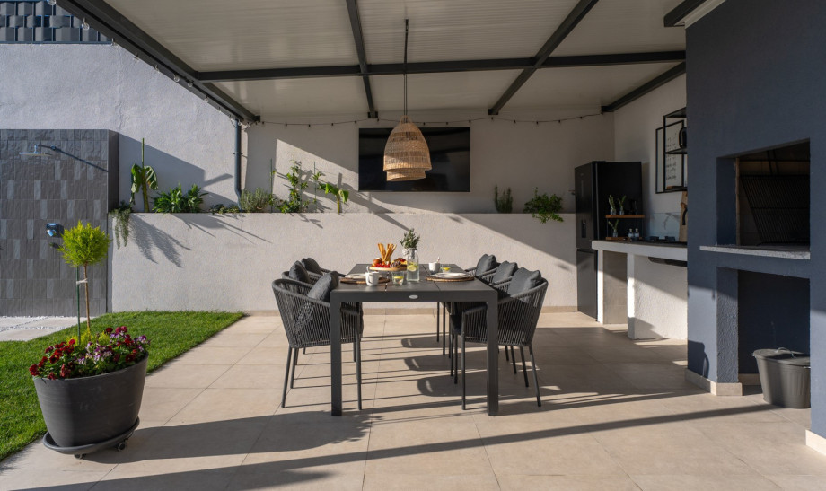 Covered al fresco dining in the fully equipped summer kitchen with a TV and traditional barbecue.