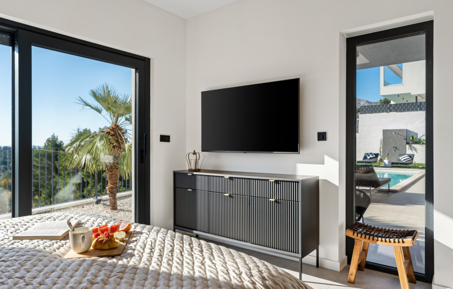 Master Bedroom view showing the wall-mounted TV and direct access to the pool area.