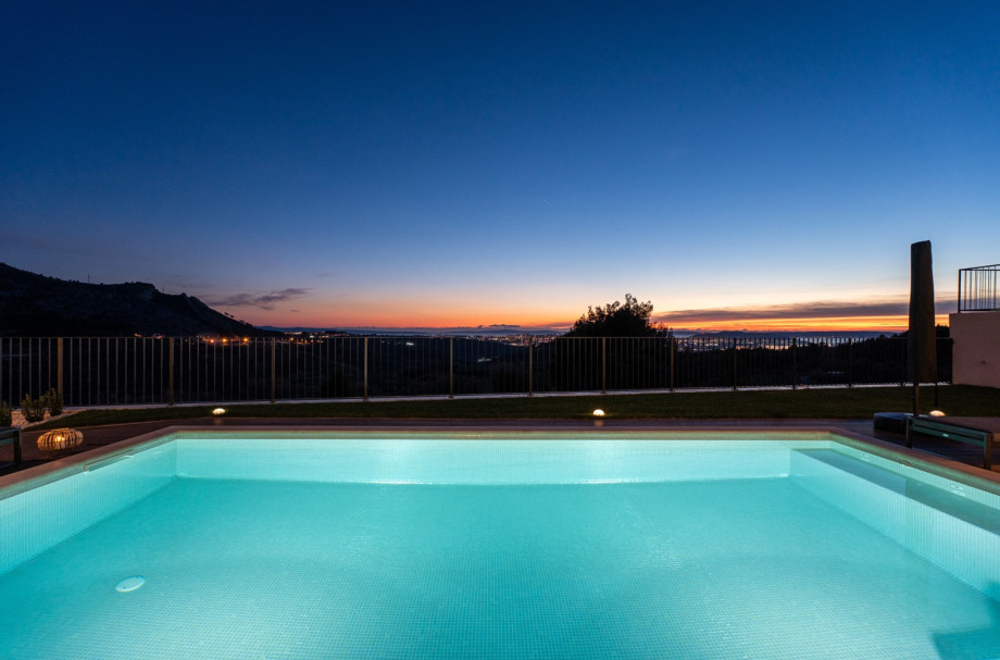 The illuminated private 8m x 4m swimming pool at twilight, with the city of Split visible in the distance.