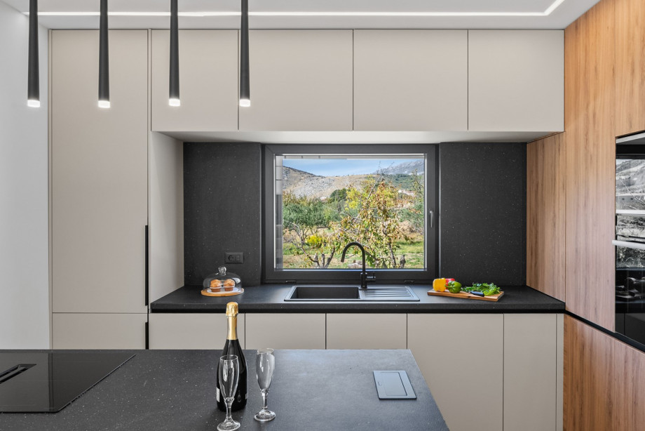 This modern kitchen features black countertops and a large window overlooking the natural surroundings.