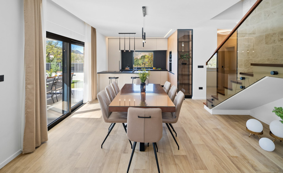 An elegant open-concept space featuring a large dining table and a stylish glass-railed staircase.