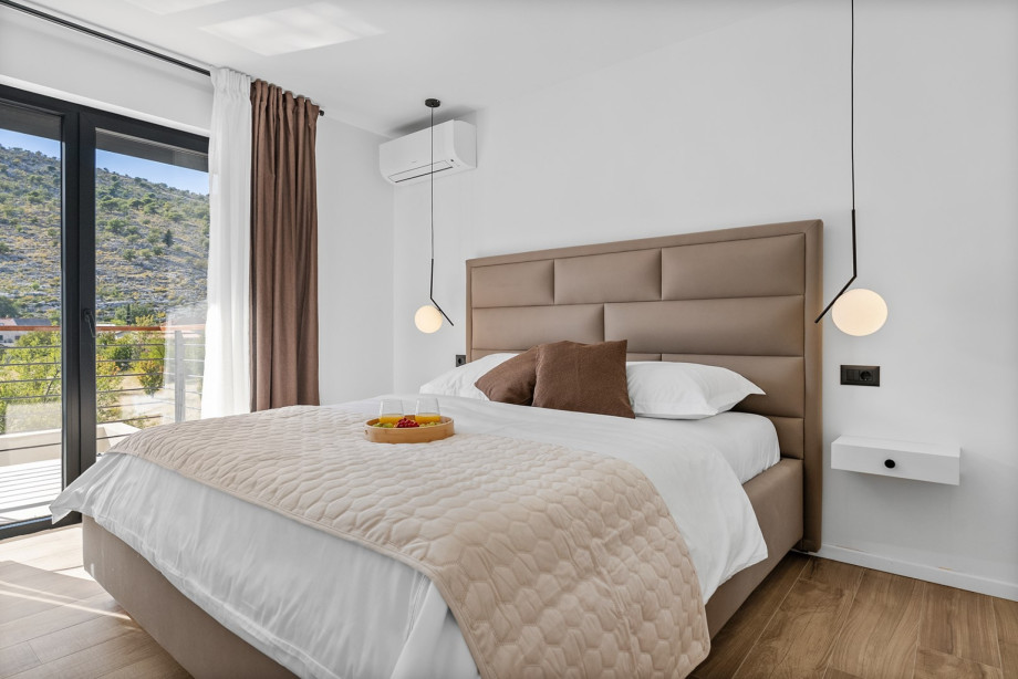 Stylish bedroom with a king-size bed, modern lighting, and access to a scenic balcony.