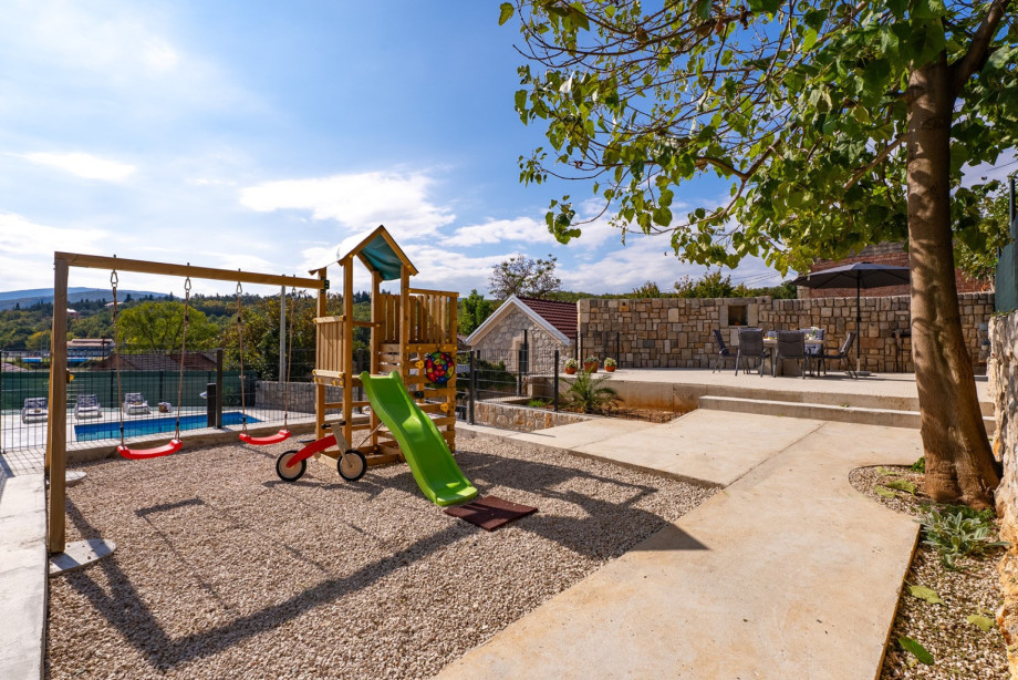 The kids' climbing frame with a slide and swing is nestled beneath a tree, offering a fun-filled space for the younger guests.