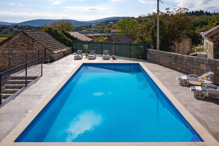 The large, blue private swimming pool is surrounded by a tiled patio, perfect for cooling off during hot summer days.