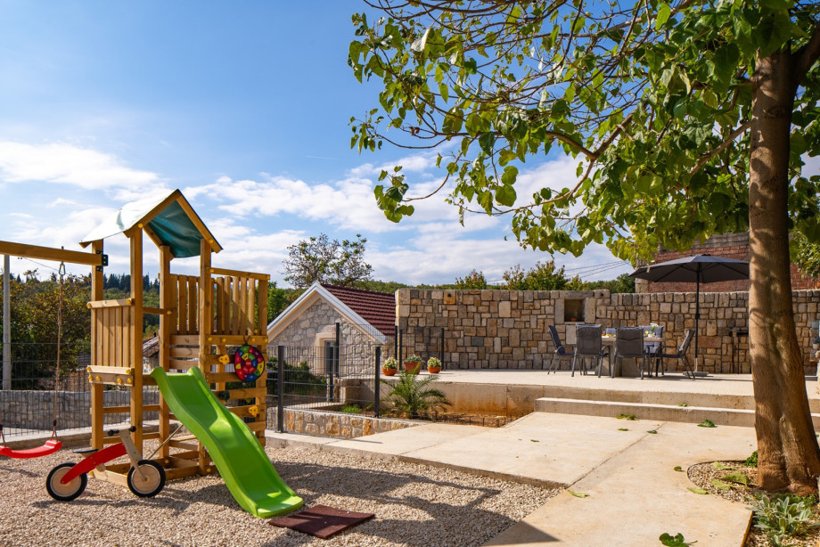 The outdoor paradise includes a kids' climbing frame with a slide and swing nestled beneath a tree, offering fun for families.