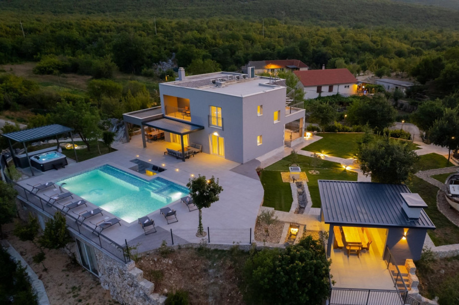 Evening shot of the lit-up villa and 66 sqm pool, showing the large private garden and quiet hills.