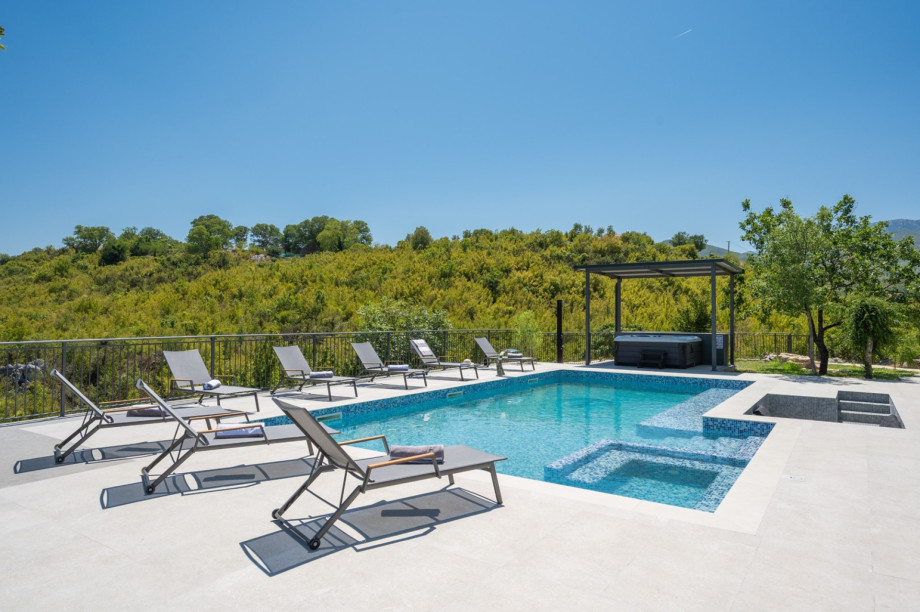 Pool deck with loungers and a covered hot tub, offering clear views of the surrounding nature.