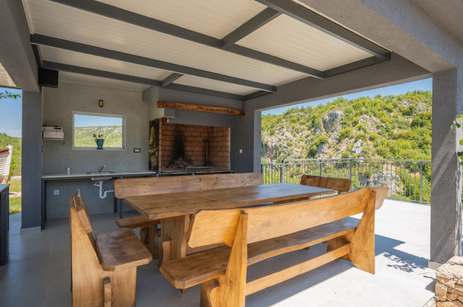 Covered dining area with traditional and gas BBQs, a fridge, sink, and views of the surrounding hills.