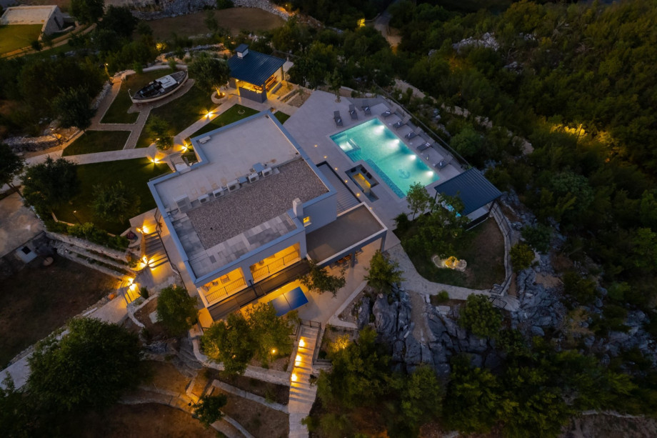 A nighttime aerial view shows the illuminated 1,900 sqm private plot and the surrounding natural environment.