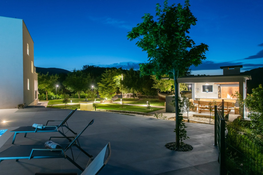 The outdoor area features a sun deck with lounge chairs and a covered summer kitchen.