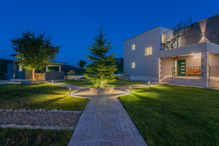 Paved walkways connect the main house to the grassy area and outdoor dining corner.