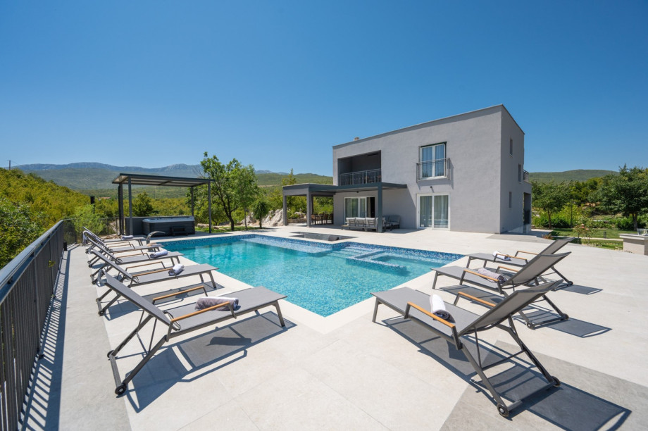 Modern villa with a spacious patio, heated pool, and several shaded outdoor lounge areas.