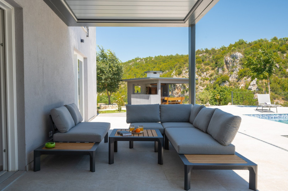 A covered lounge corner with a comfortable sofa is located next to the pool.