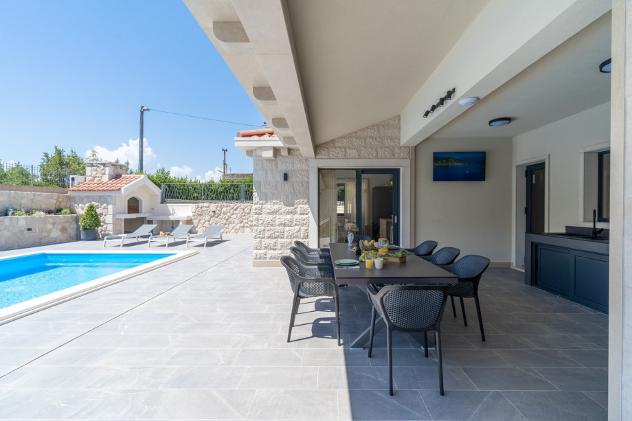 Covered outdoor dining area with summer kitchen and a TV, and a traditional barbecue