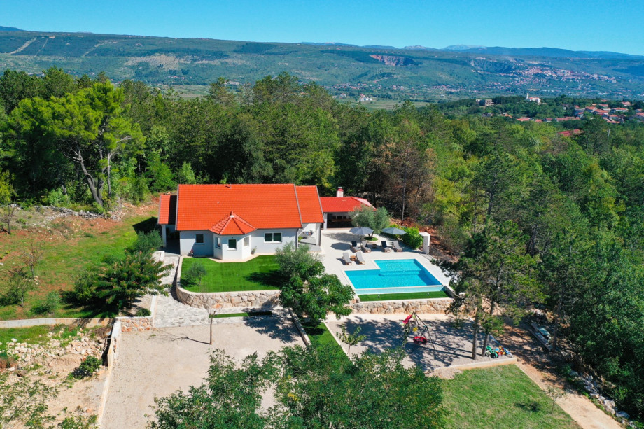 An aerial view shows the 250 sqm villa, the expansive pool, and a grassy plot with a swing and slide for children.