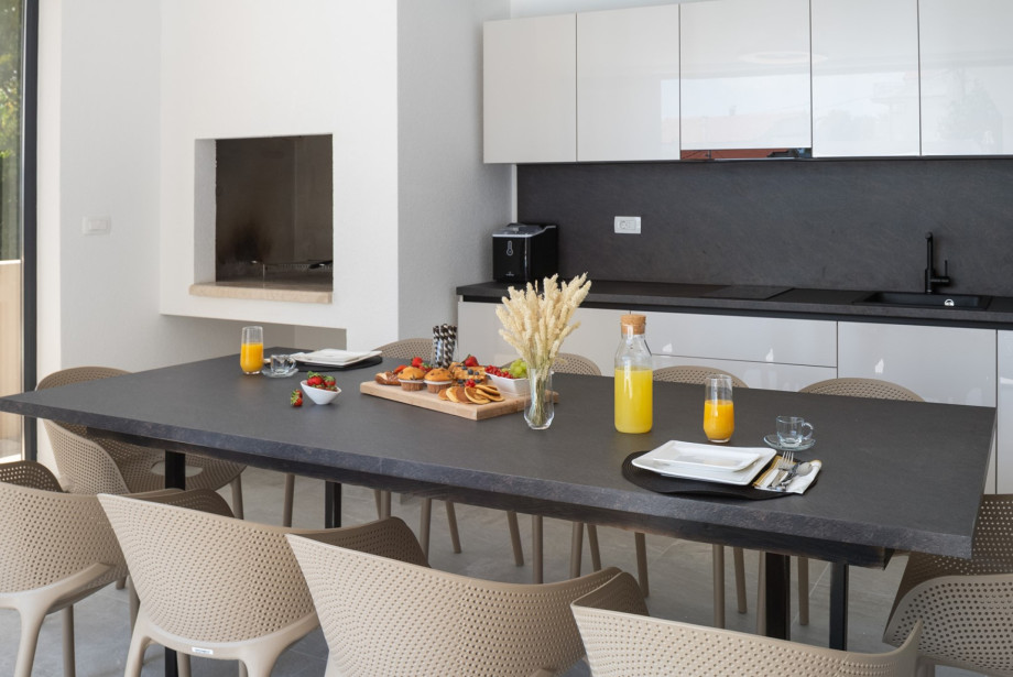 Covered outdoor dining area with a traditional wood/charcoal barbecue and a spacious table for 10 people