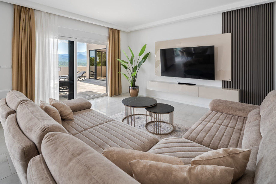 Comfortable sofas are arranged around a flat-screen TV, while large glass doors lead directly to the pool area, blending indoor and outdoor living seamlessly