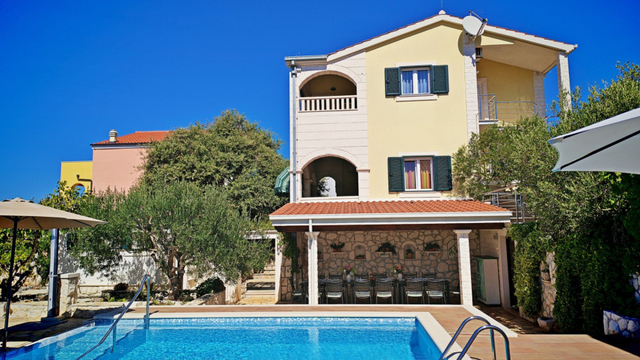 The villa's main building, featuring three separate apartments and an arched balcony, overlooks the pool area and the outdoor dining space.