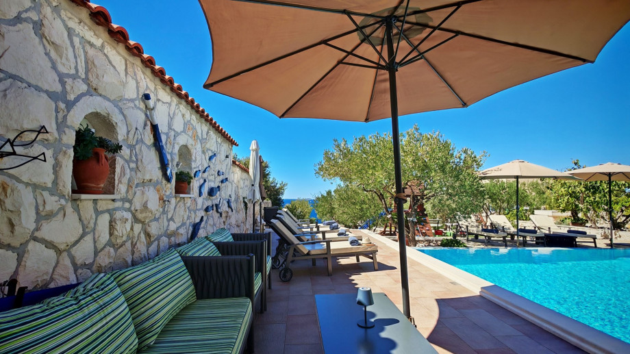A cosy lounge corner with striped cushions is set against a charming stone wall, offering a shaded retreat right next to the pool area.