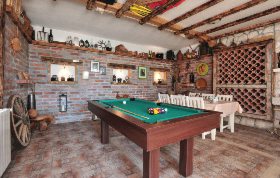 The billiard room (34 sqm) provides indoor entertainment with a pool table, an extra dining table, and a rustic decor featuring a large wine rack.