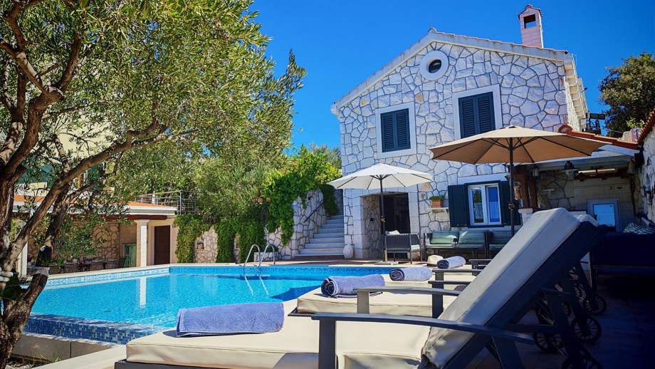 The traditional stone-clad facade of the villa offers a charming, Mediterranean ambience right next to the pool area with comfortable sun loungers.