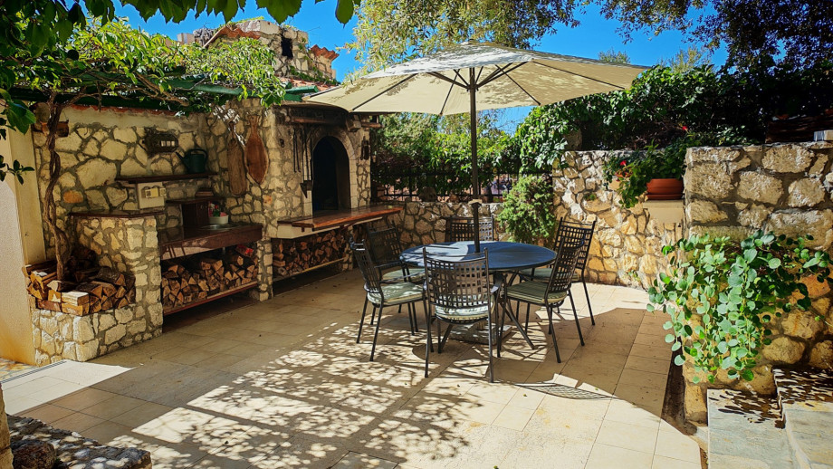 A dedicated charcoal/wood barbecue area is surrounded by stone walls, offering a shaded, traditional spot for outdoor cooking and dining.