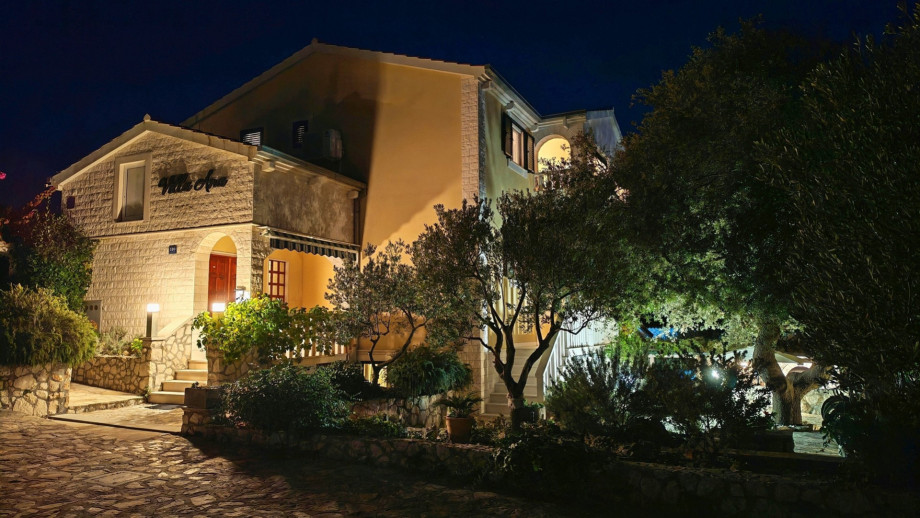 The villa exterior at night shows the warm glow from the windows, emphasising the stunning two-story structure and surrounding vegetation.