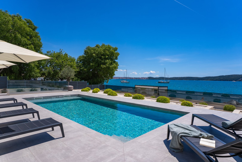 A stylish waterfront villa with a private pool and elegant sun loungers