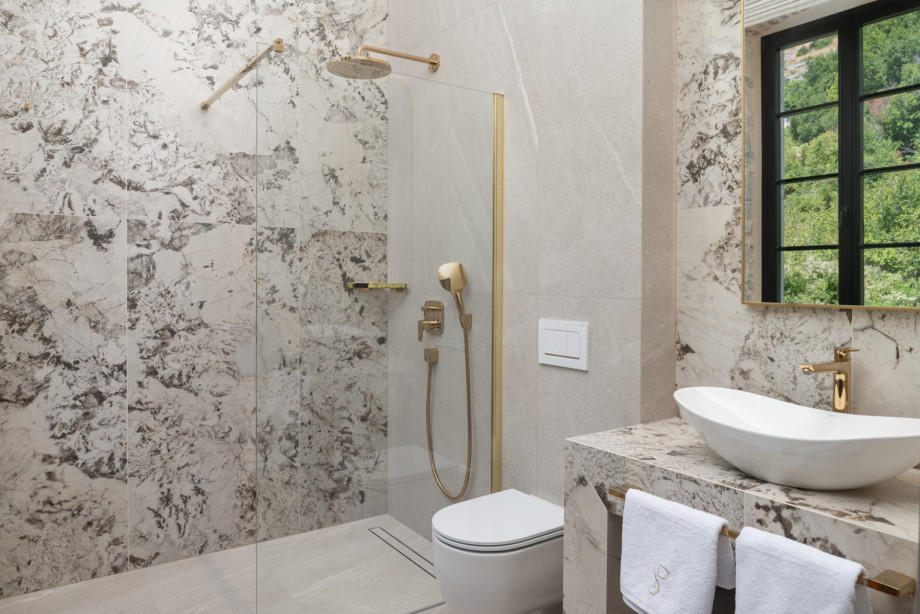 An elegant en-suite bathroom features a walk-in shower with premium gold fixtures and stone finishes.