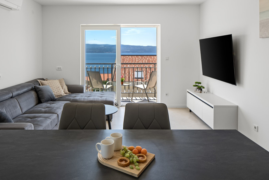 Open-concept living area with a TV, and a balcony that overlooks the sea