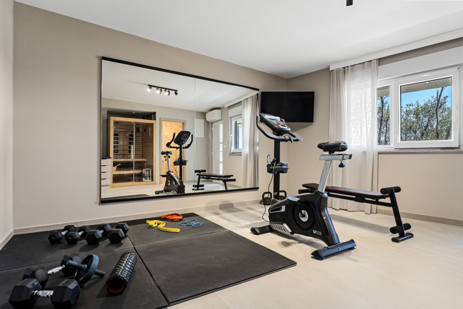 Descending to the lower ground floor, guests can unwind in the wellness area: a Finnish and infrared sauna, a gym equipped with a treadmill, exercise bike, and a range of weights