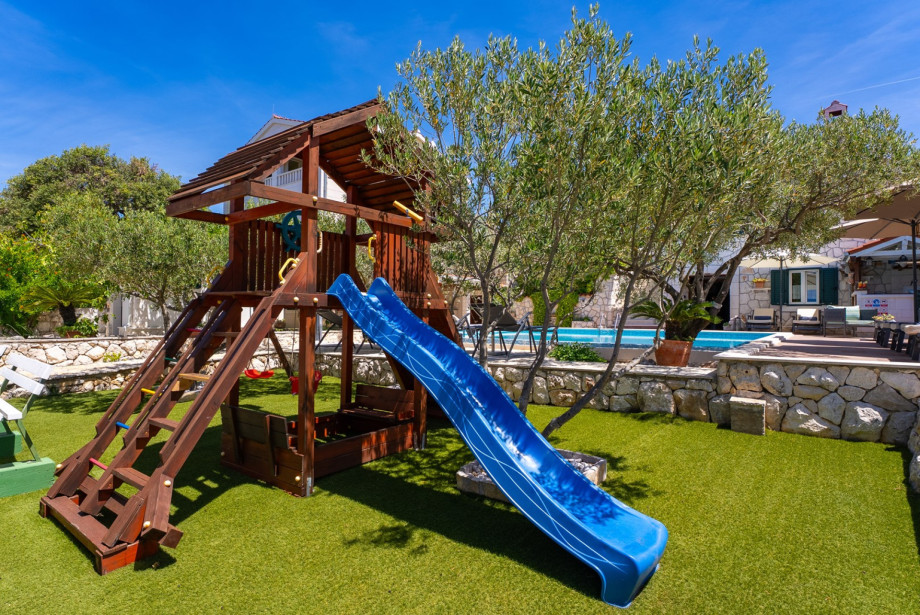 The kids play area includes a climbing frame, a slide, and a trampoline.
