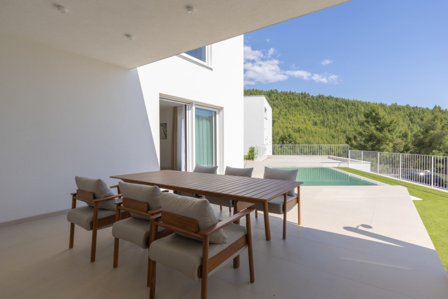 Covered outdoor dining terrace with high-quality designer teak furniture from Fjaka, overlooking the private pool and Mediterranean greenery