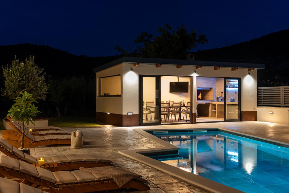 Covered outdoor dining area with a dining table, BBQ, and a sink is next to the pool.