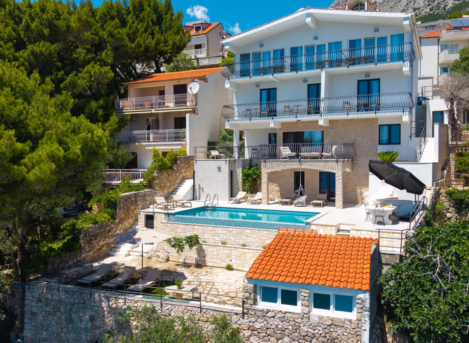 An outdoor staircase leads directly from the lower terrace down to the pebble beach.