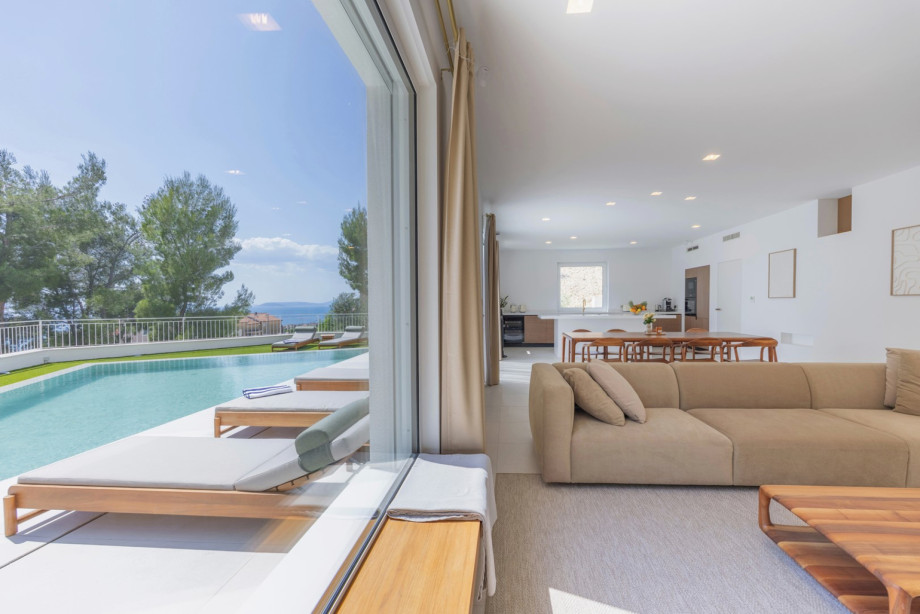 Bright open-plan living room with refined furniture from Prostoria and Artisan, large windows, and beautiful views of the sea and greenery