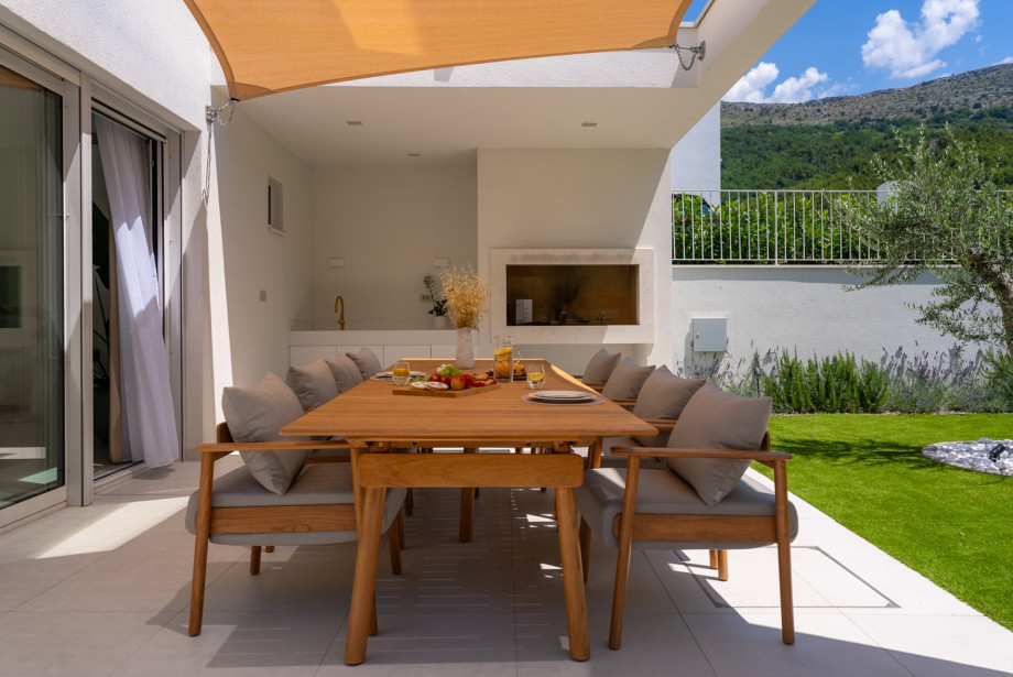 Covered exterior dining terrace with high-quality designer teak furniture from Fjaka and an outdoor fireplace