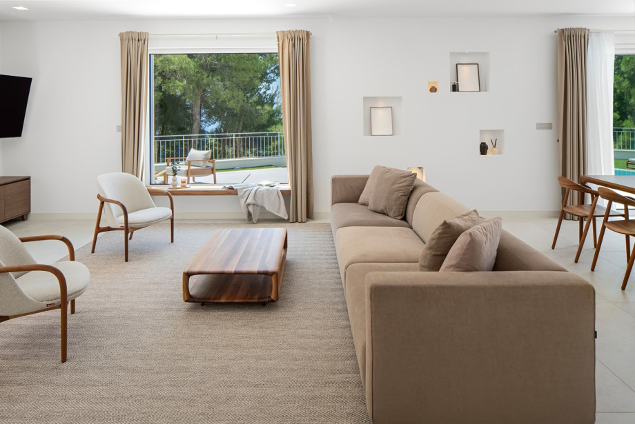 Cozy living room corner with refined furniture from Artisan, framed by a large window overlooking the pool, pine trees, and sea