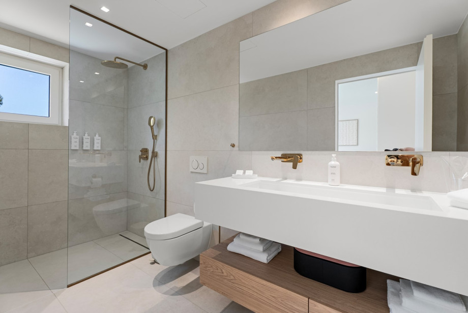 An en-suite bathroom with a shower, double sink, and a toilet