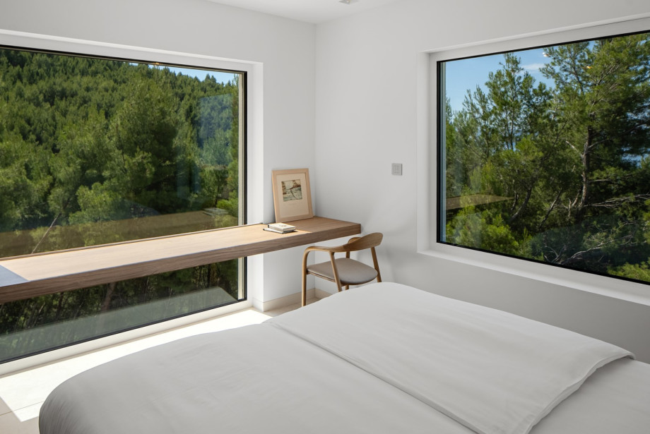 Bright bedroom with large windows overlooking pine trees  and Mediterranean greenery
