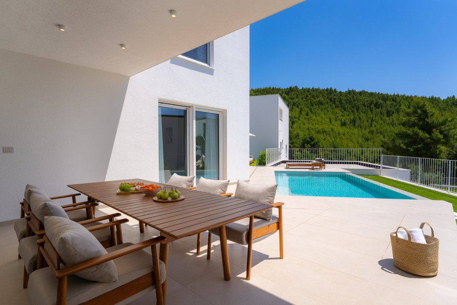 Überdachte Terrasse mit Essbereich im Freien und hochwertigen Teakholzmöbeln von Fjaka, mit Blick auf den privaten Pool und das mediterrane Grün