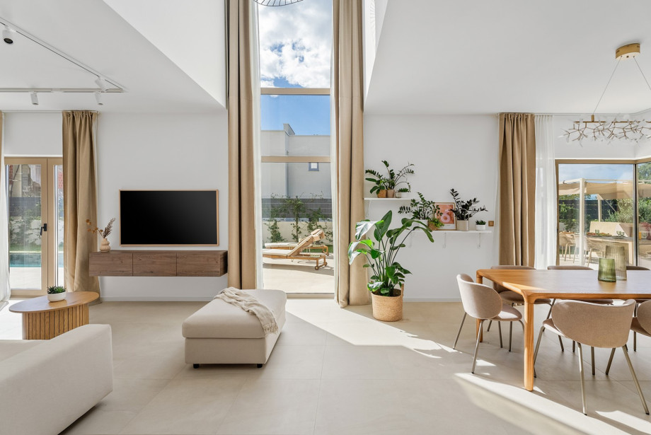 A large living area features a cozy sofa, a flat-screen TV with surround sound, and a glass wall that provides a view of the pool area